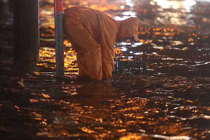 Công nhân thoát nước đội mưa vớt rác giúp thông dòng chảy trên đường Nguyễn Duy Trinh, chiều 27/12. Ảnh: Quỳnh Trần