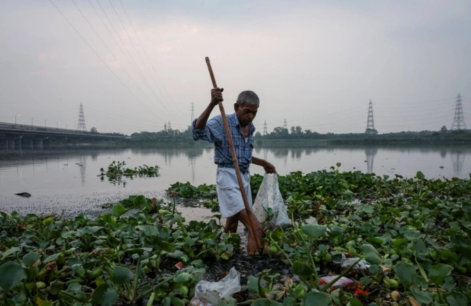 Ông Gupta, 67 tuổi, mò tiền xu, đồ giá trị ở ven sông Yamuna, ngày 26/6. Ảnh: Reuters