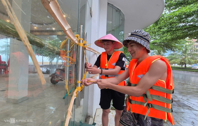 Hai thanh niên gia cố cửa hàng trên đường Hồ Xuân Hương, phường Sầm Sơn, trưa 21/7. Ảnh: Lê Hoàng