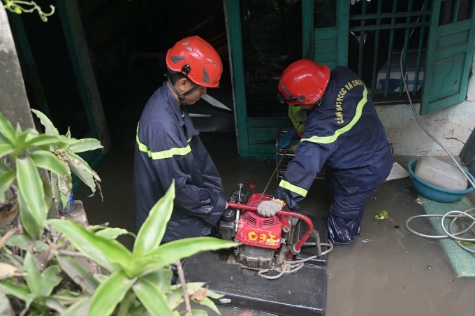 Cảnh sát PCCC kéo máy bơm vào hộ dân bị ngập sâu gần một mét để bơm thoát nước. Ảnh: Đình Văn