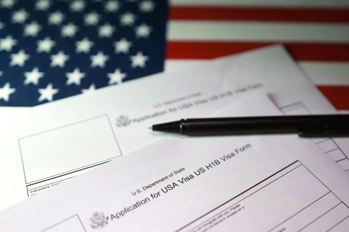 Mẫu điền đơn xin visa H-1B trên nền cờ Mỹ. Ảnh: Reuters