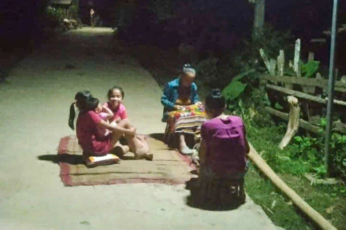 Nhà mất điện, các cụ bà tập trung ra đường lấy ánh sáng đèn năng lượng mặt trời để thêu váy. Ảnh: Bùi Châu