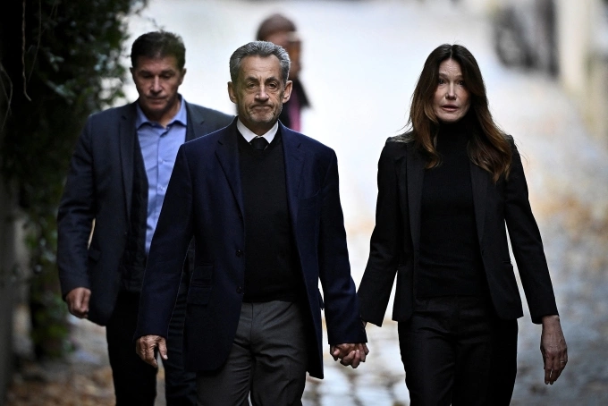 Ông Sarkozy nắm tay vợ, ca sĩ Carla Bruni khi rời nơi cư trú. Ảnh: AFP