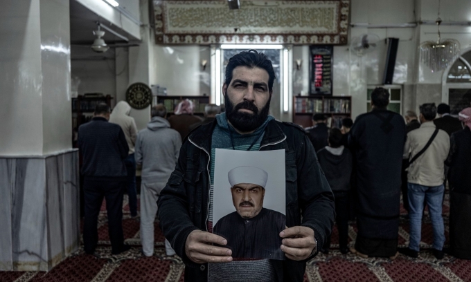 Con trai cả của giáo sĩ Abdu Kharouf, người đã qua đời trong một nhà tù ở Damascus, cầm trên tay bức ảnh cha mình. Ảnh: WSJ