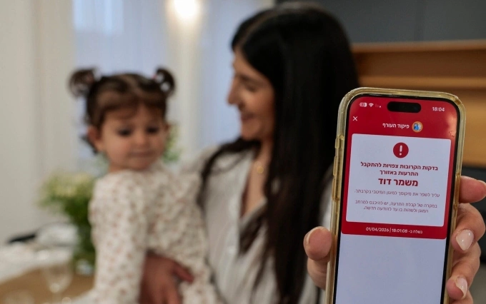 Người mẹ bế con chia sẻ tin nhắn cảnh báo tên lửa tại Mishmar David, Israel, ngày 1/4. Ảnh: Flash90