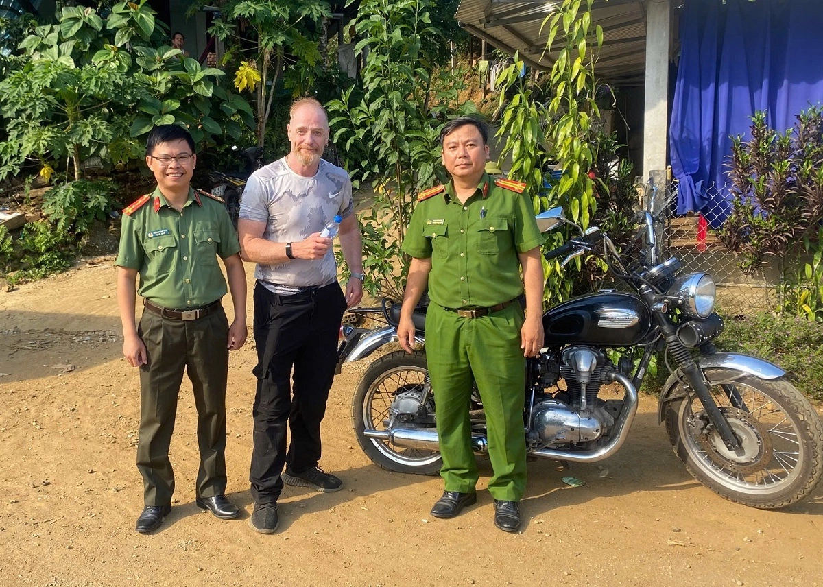 Ông Barry và Trung tá Phan Tiến Dũng, Trưởng Công an xã Đặng Thùy Trâm (phải), cùng Đại úy Phạm Trung Tiển bên chiếc xe bị thủng lốp. Ảnh: Công an xã Đặng Thùy Trâm